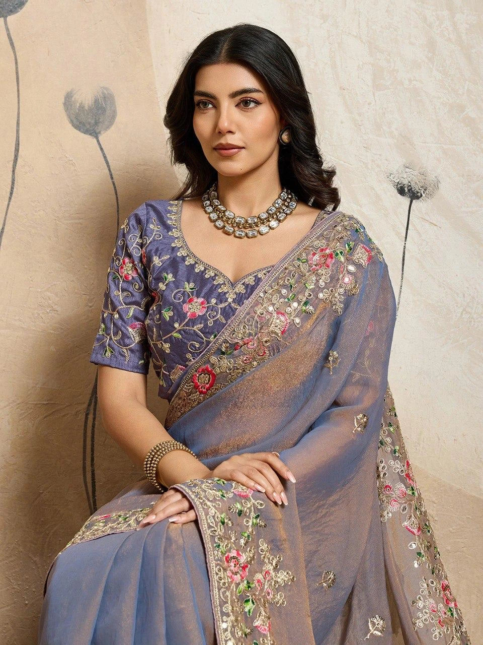 Woman wearing a blue saree with floral embroidery against a neutral background